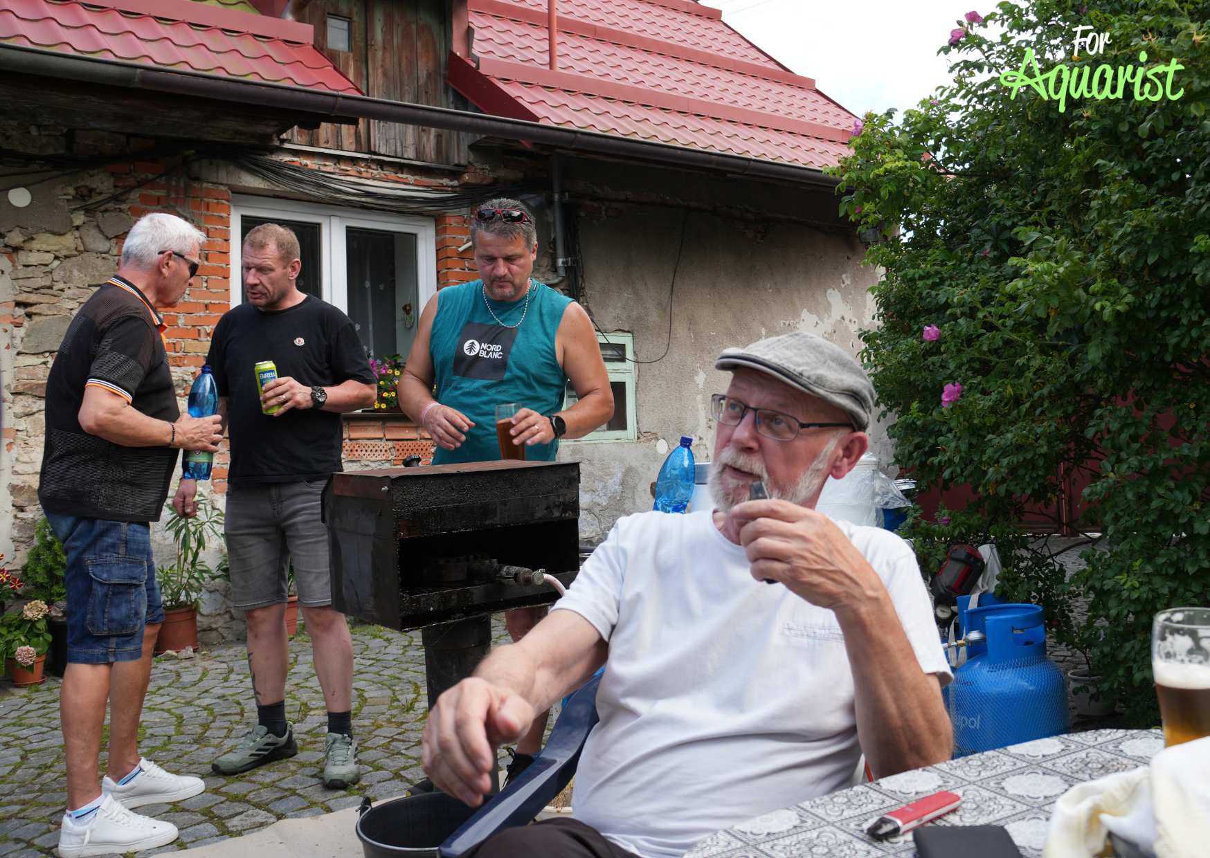 Posezení u stolečku (Luděk Zicháček) a grilování (Luboš Guhl). Diskuze v pozadí Jarda Dvořák a Jiří Kudrna.